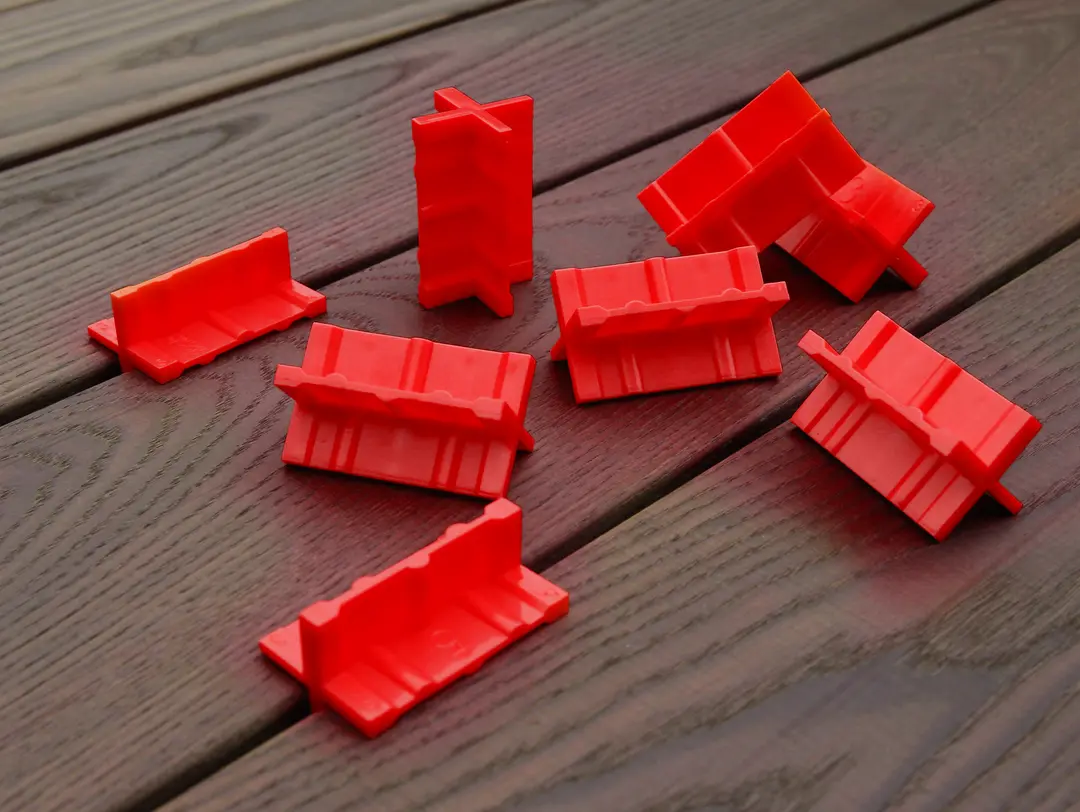 Acht Spacer Cobra® Deck 8 St., roter Kunststoff mit Rillen, auf einer Holzoberfläche, stehend oder liegend angeordnet.