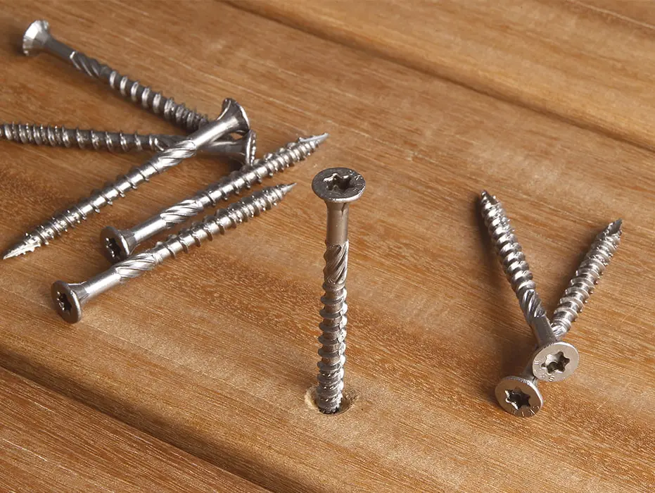 Vis Cobra Inox 6x70mm, finition acier inoxydable, posées sur bois ; une vis partiellement vissée, boîte de 100 pièces visible à l'arrière-plan.