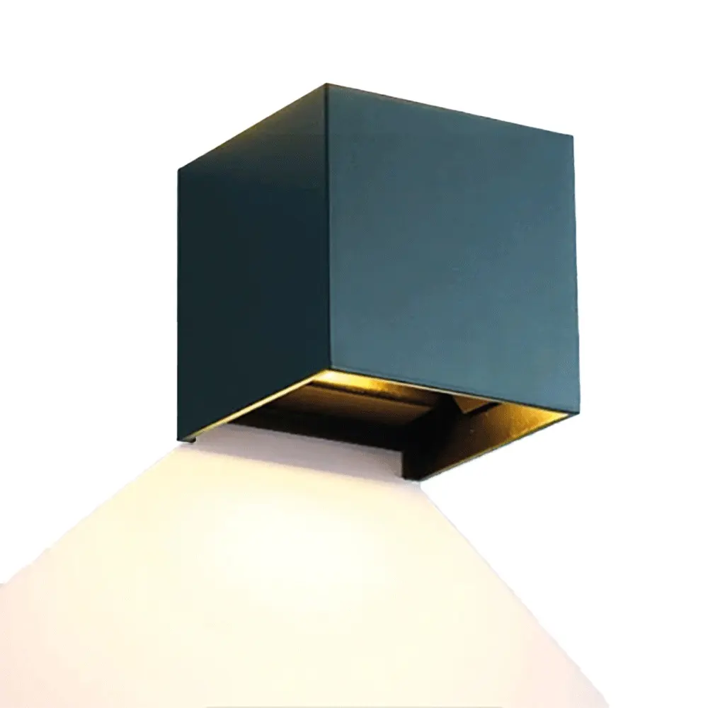 Applique murale noire en forme de cube, modèle non précisé, en métal, diffusant la lumière vers le bas sur une surface blanche, fond blanc uni.